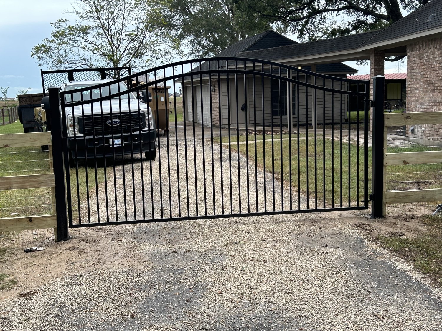 Arched black metal double driveway gate on a gravel drive — Jorge Torres Fence, Houston