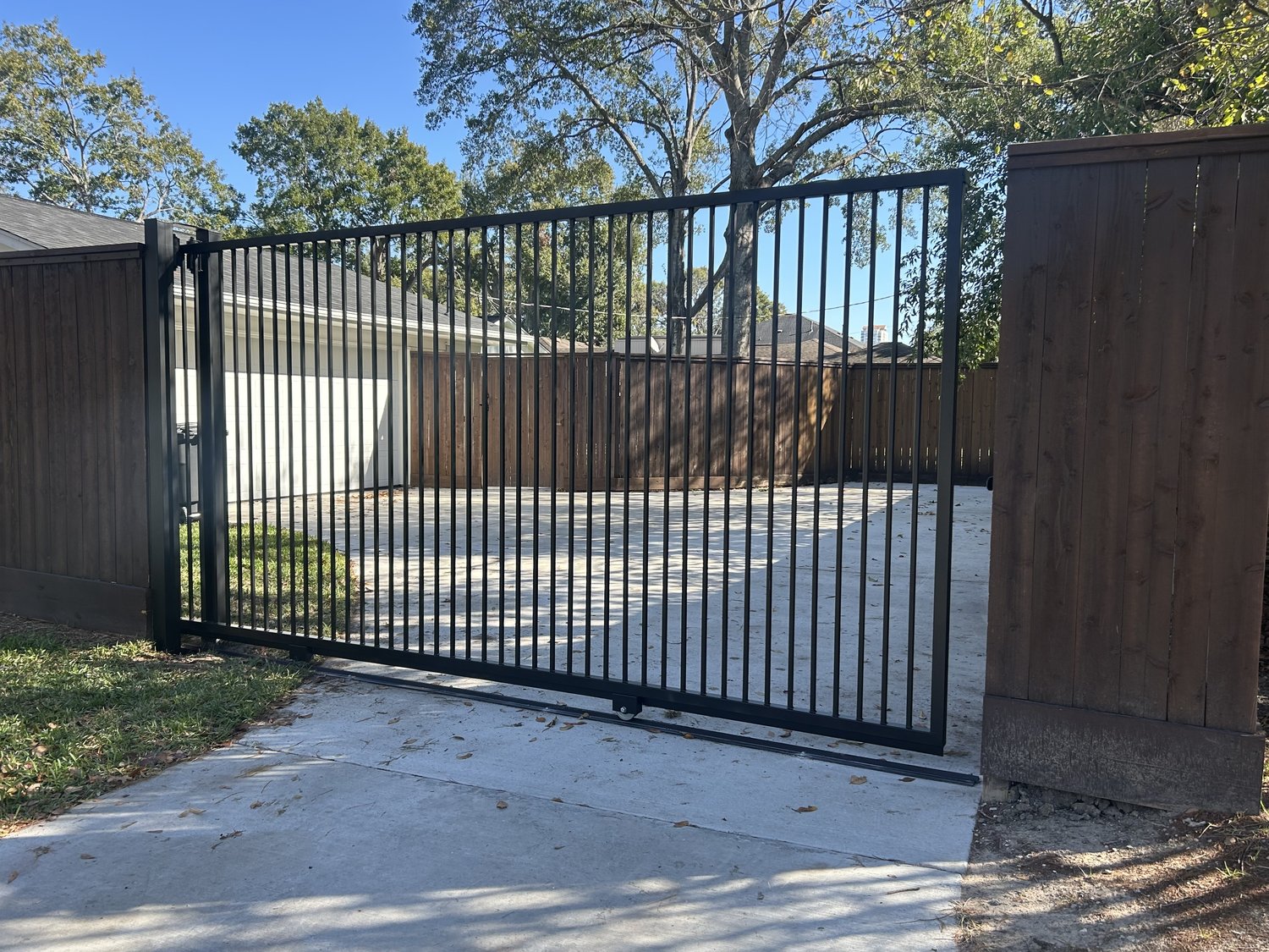 Black metal sliding driveway gate with stained wood fence — Jorge Torres Fence, Houston