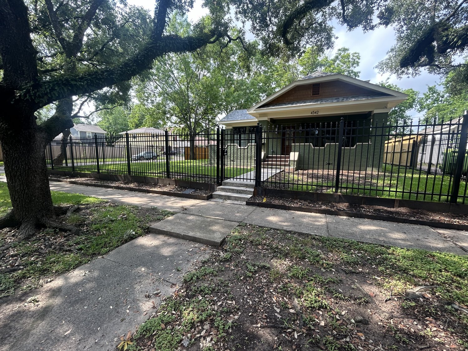 Black iron fence framing a Houston bungalow front yard with oak trees — Jorge Torres Fence